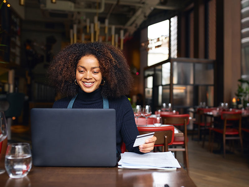 Person sitting down looking at a laptop holding their debit card